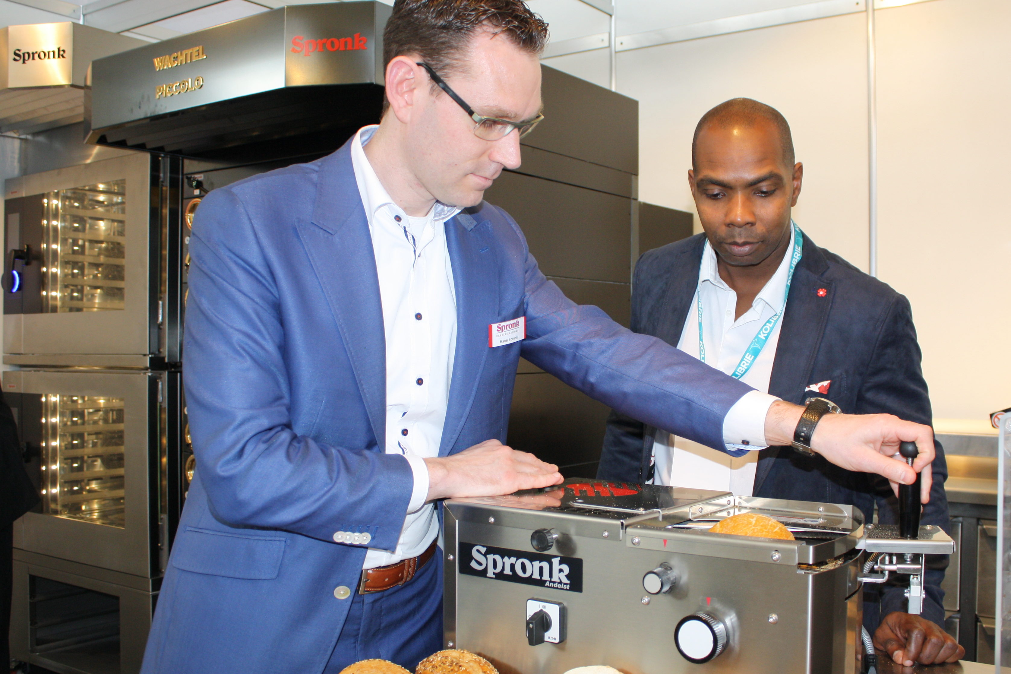 Harm Spronk (links) legt een bezoeker de werking van de broodjessnijmachine uit.

Foto: AMR