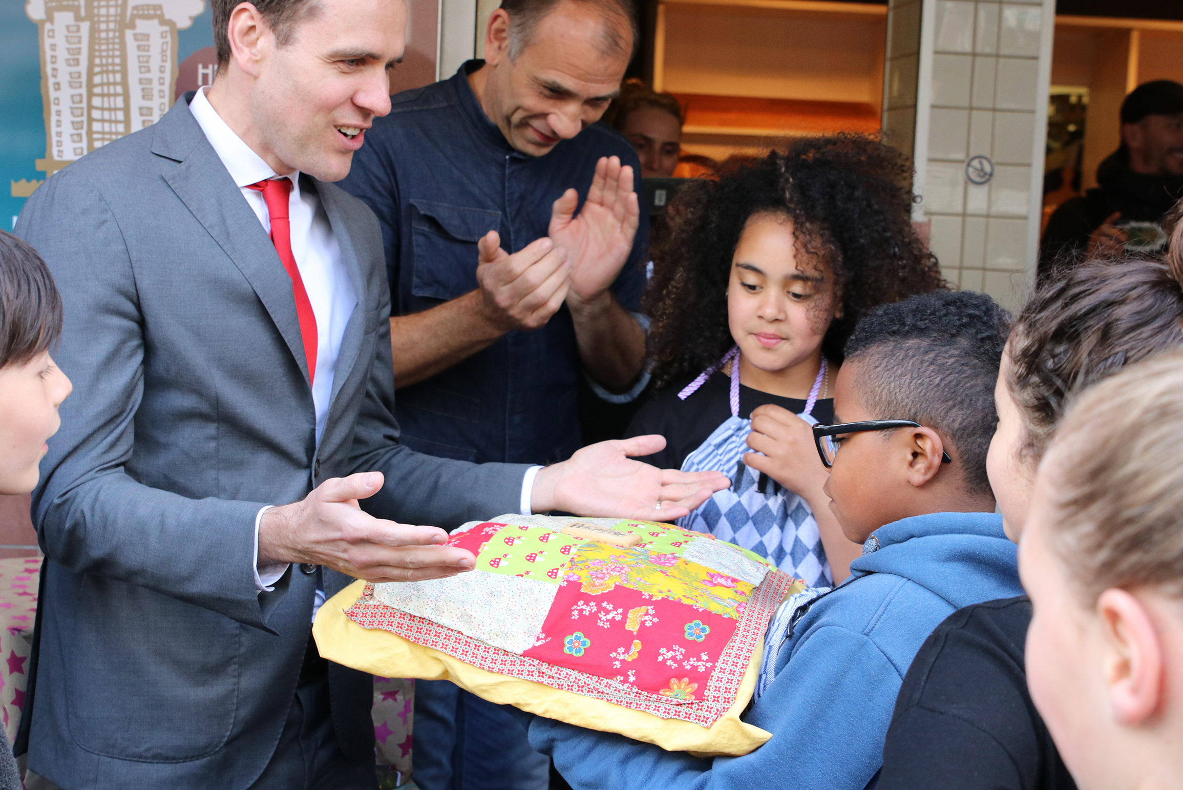 Amsterdam-Zuid-bestuurder Marijn van Ballegooijen neemt het Wolkenkrabbertje in ontvangst van de RijnBIZkids. Bakker Remko applaudisseert op de achtergrond.

Foto: Carla Termorshuizen