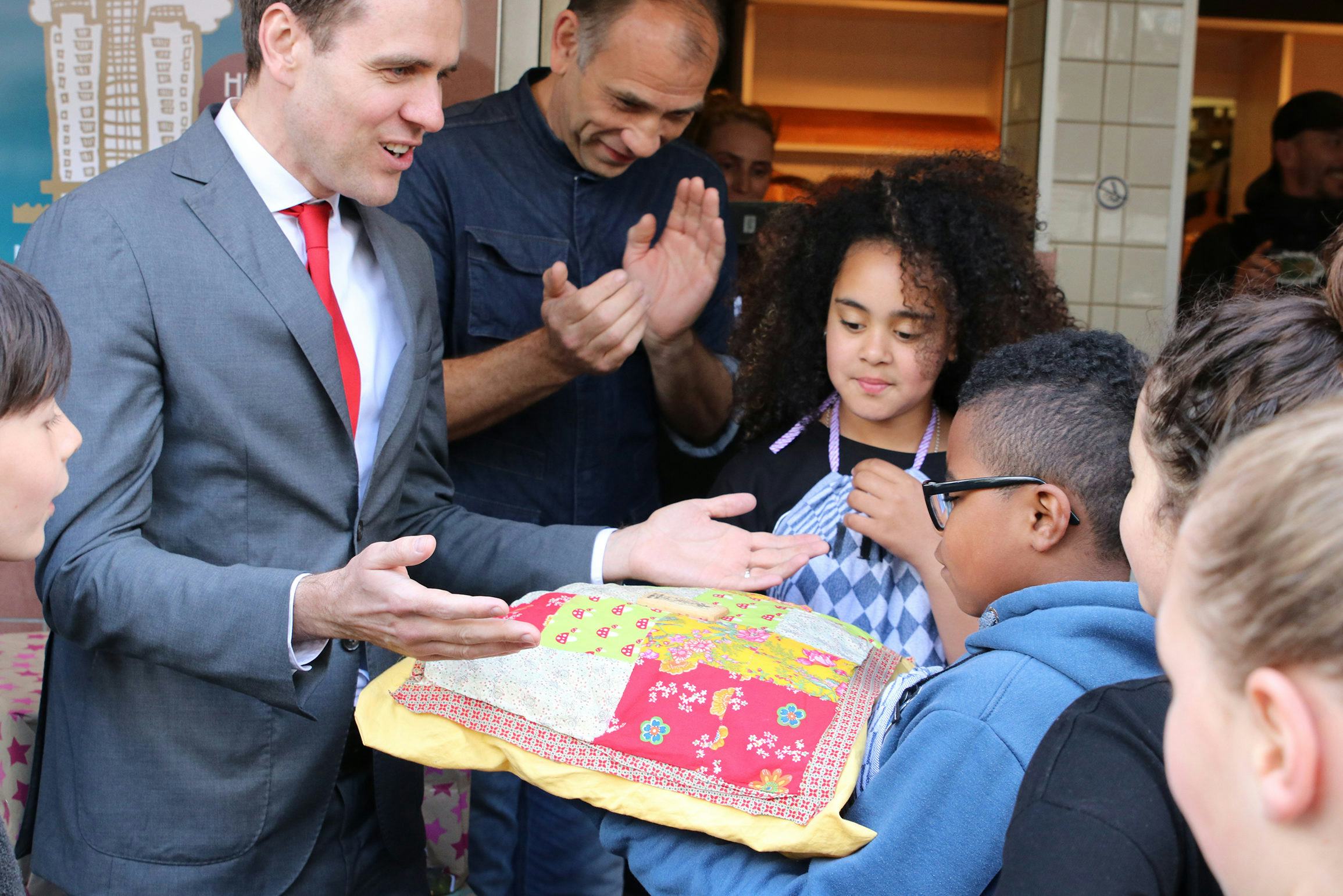Amsterdam-Zuid-bestuurder Marijn van Ballegooijen neemt het Wolkenkrabbertje in ontvangst van de RijnBIZkids. Bakker Remko applaudisseert op de achtergrond.
Foto: Carla Termorshuizen