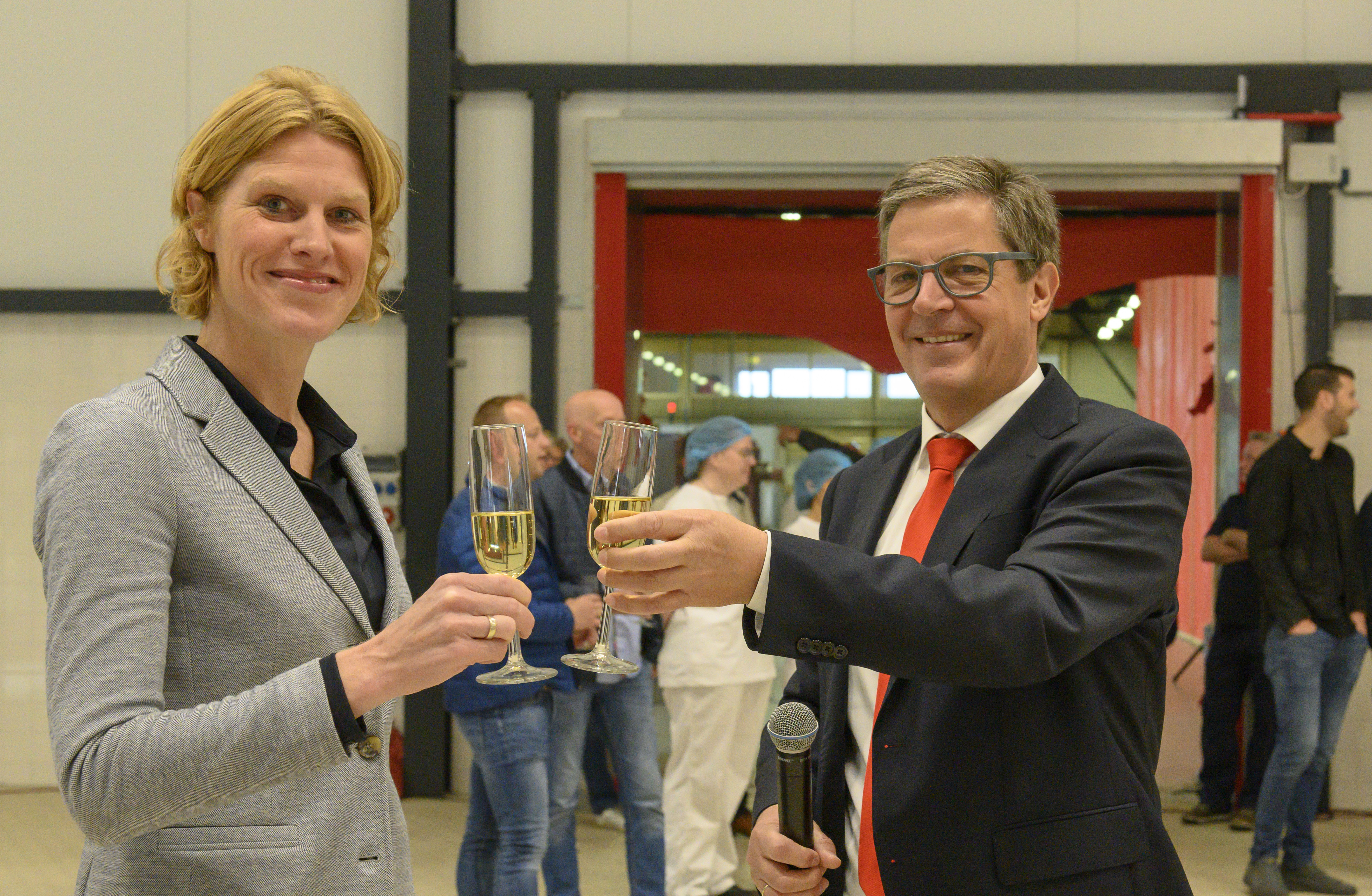 Wethouder Caroline de Pee en Royal Steensma-directeur Rimmert de Jong toasten op de opening van de nieuwe drooghal van Royal Steensma in Franeker. De oude hal werd vorig jaar door een fikse brand verwoest.