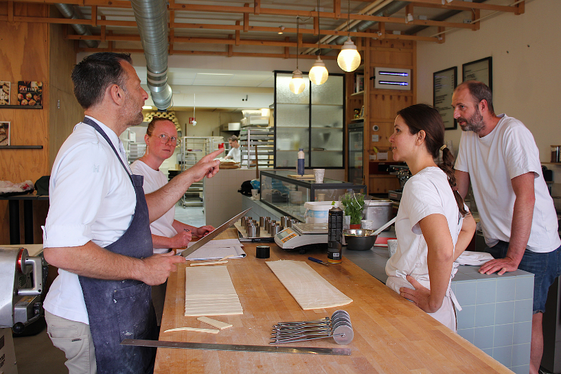 Docent Hans Heiloo (links) geeft aan het team van Mattijs (r) in de bakkerij van Water & Bloem concrete aanwijzingen voor verbeteringen. Foto's: Bakery Institute