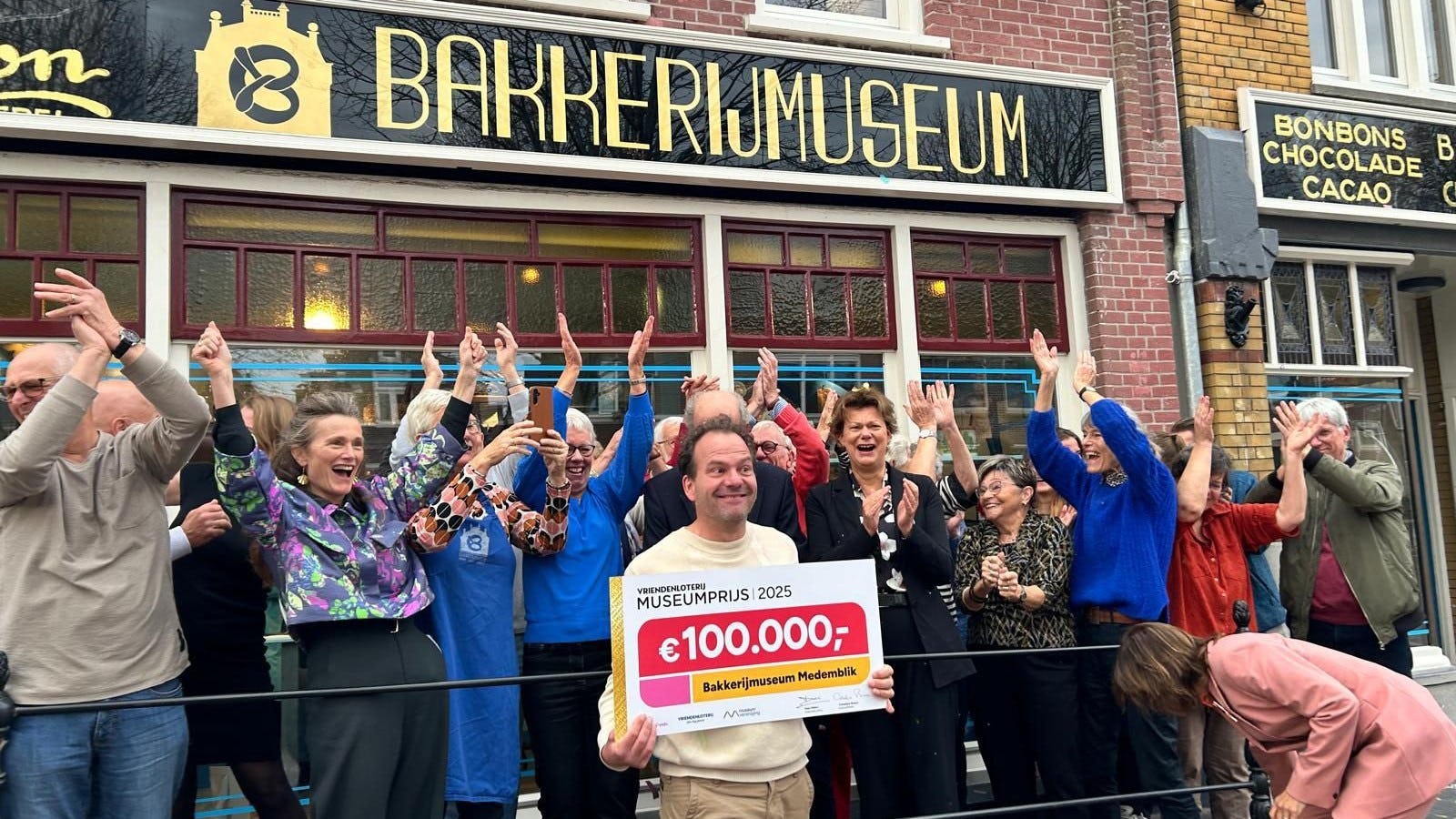 Directeur Jacco Spil van het bakkerijmuseum neemt de prijs in ontvangst, terwijl het team joelt.