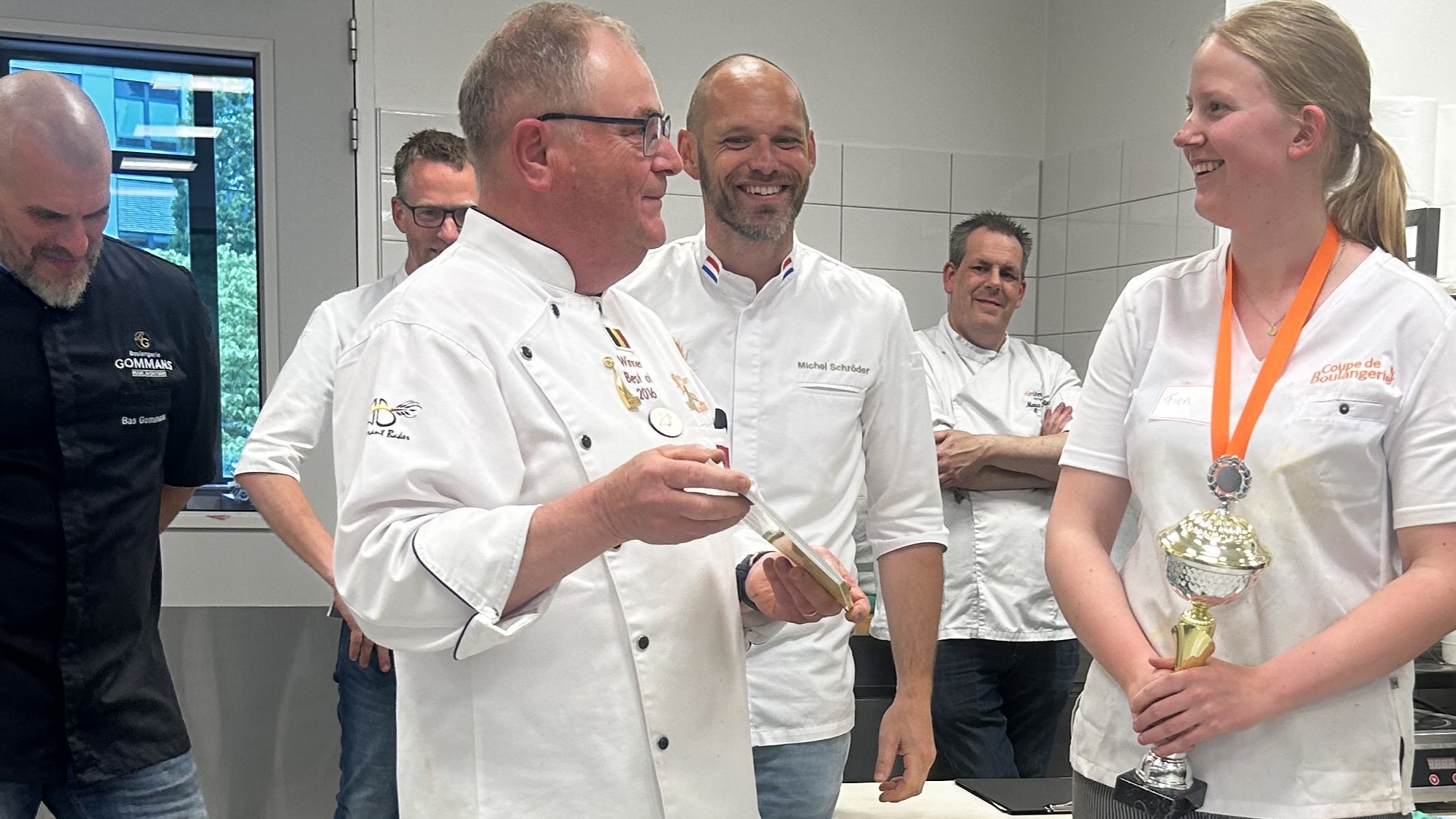 Winnares Fien Kwant wordt lovend toegesproken door jurylid Guido Devillé (wereldkampioen Mondial du Pain 2016), terwijl de andere juryleden meeluisteren. 
